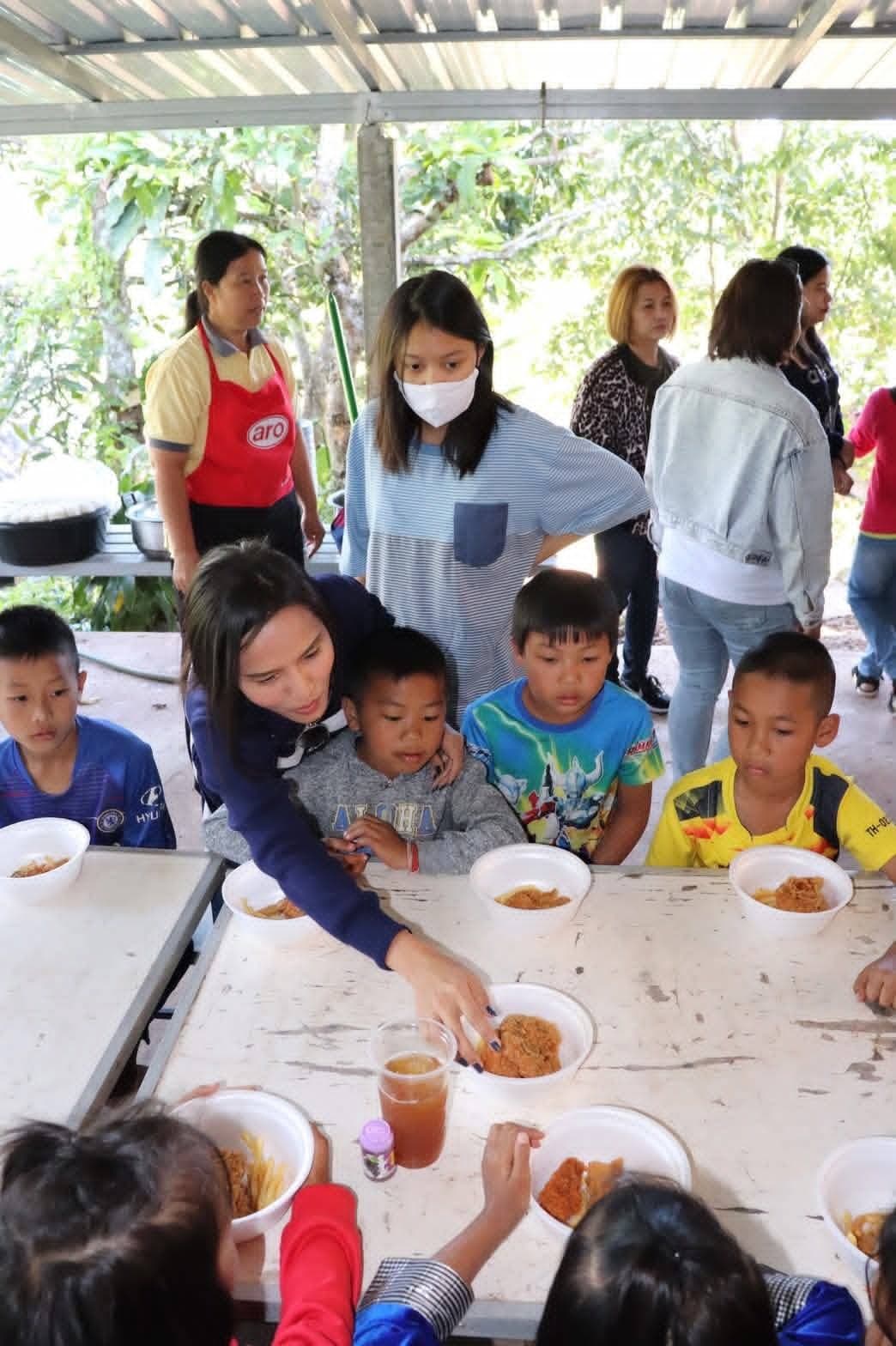 Children receiving meals at a weathered table under a metal roof in the mountains