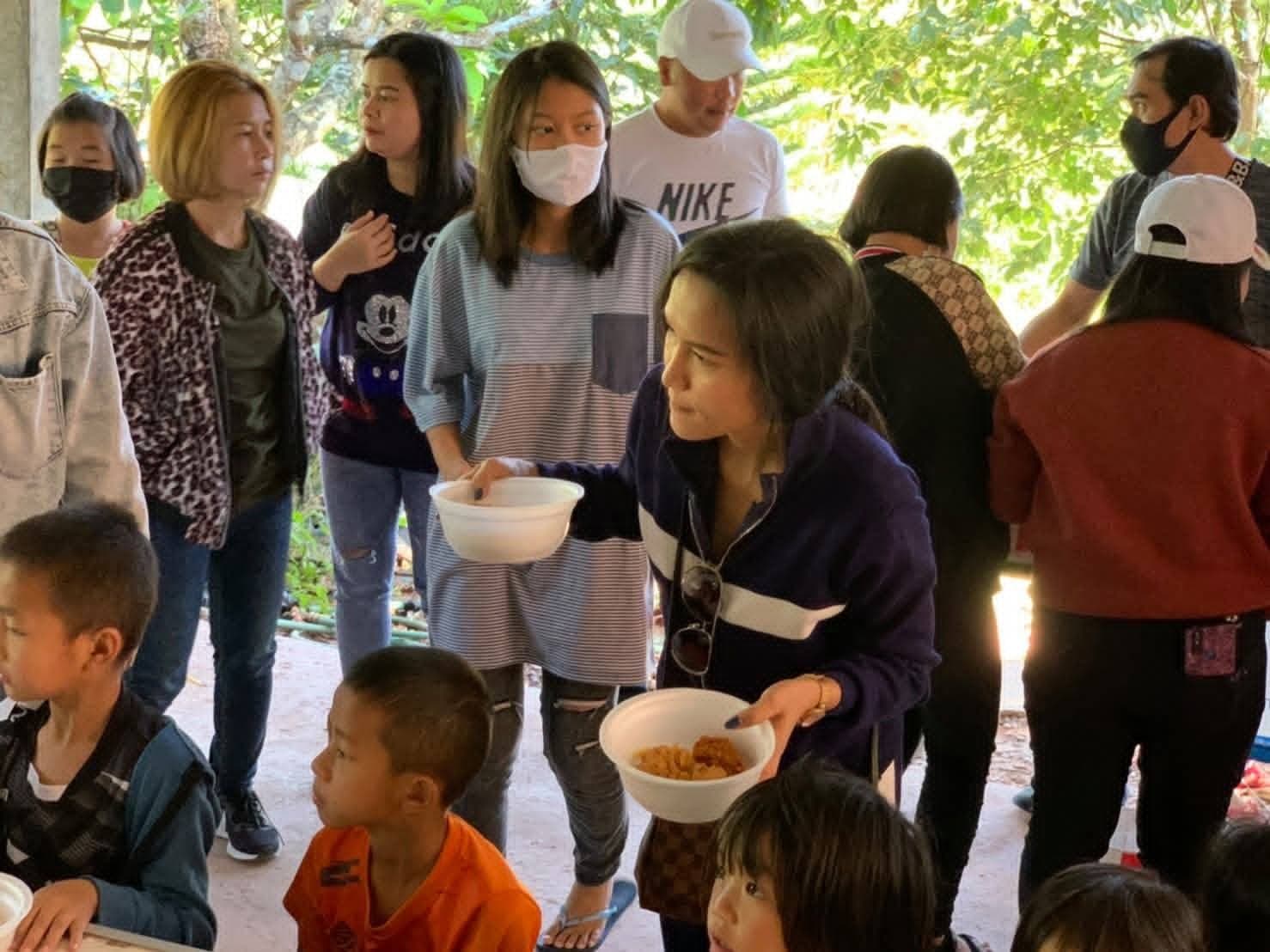 Volunteers in face masks carrying bowls of food to children during COVID relief