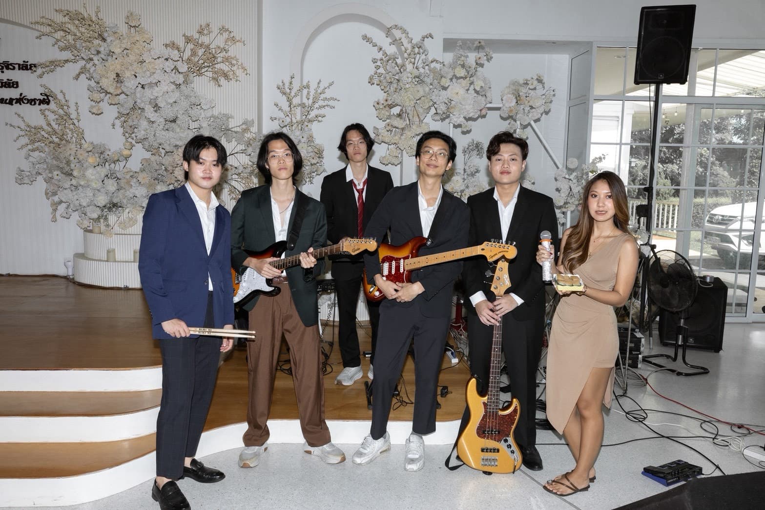 The ceremony band posing with instruments in front of white floral arrangements