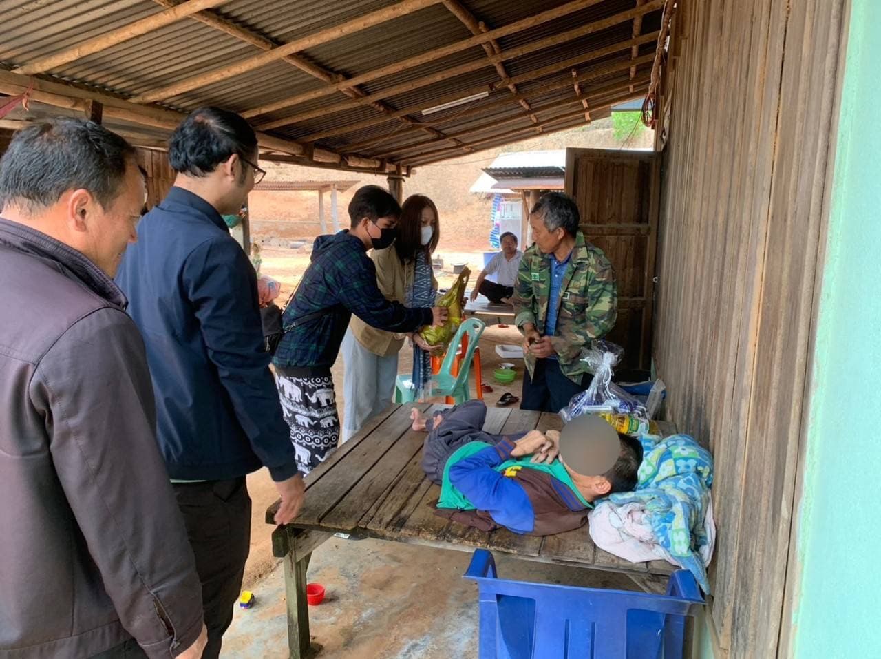 A volunteer handing a bag of rice to a resident on a wooden porch in the mountains