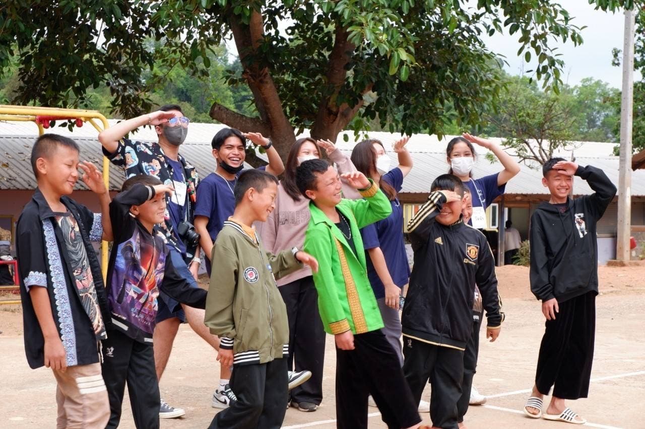 Volunteer teachers and schoolchildren posing together on a dirt playground in the highlands